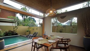 Un espace repas avec une piscine, des meubles en bois et de grandes fenêtres.