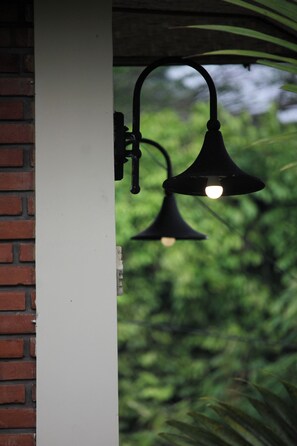 En svart utomhuslampa som är monterad på en vit pelare, med en suddig grön bakgrund.