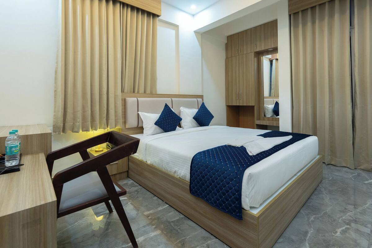 A hotel room with a bed, a desk, a chair, a water bottle, and a mirror.