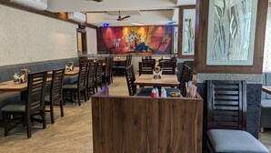 Een restaurant met houten tafels en stoelen, een centraal houten toonbankje en een muurschildering op de achterwand.