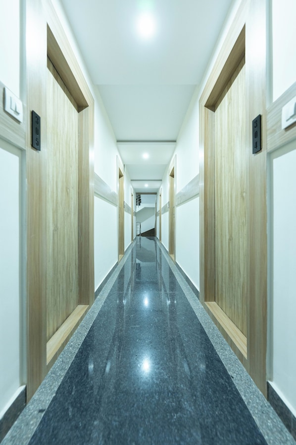 A long, narrow hallway with wooden doors on either side and a polished black floor. - Adhidhani Boutique Hotel (Bengaluru)
