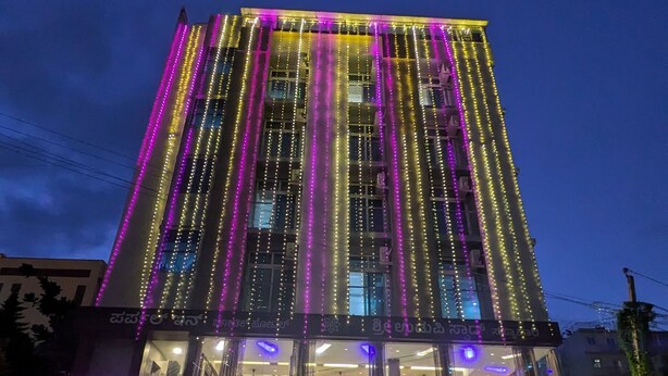 Een hotel met verticale lichtstroken en borden met 'Purple Inn' en 'Sri Udupi Swaad'.