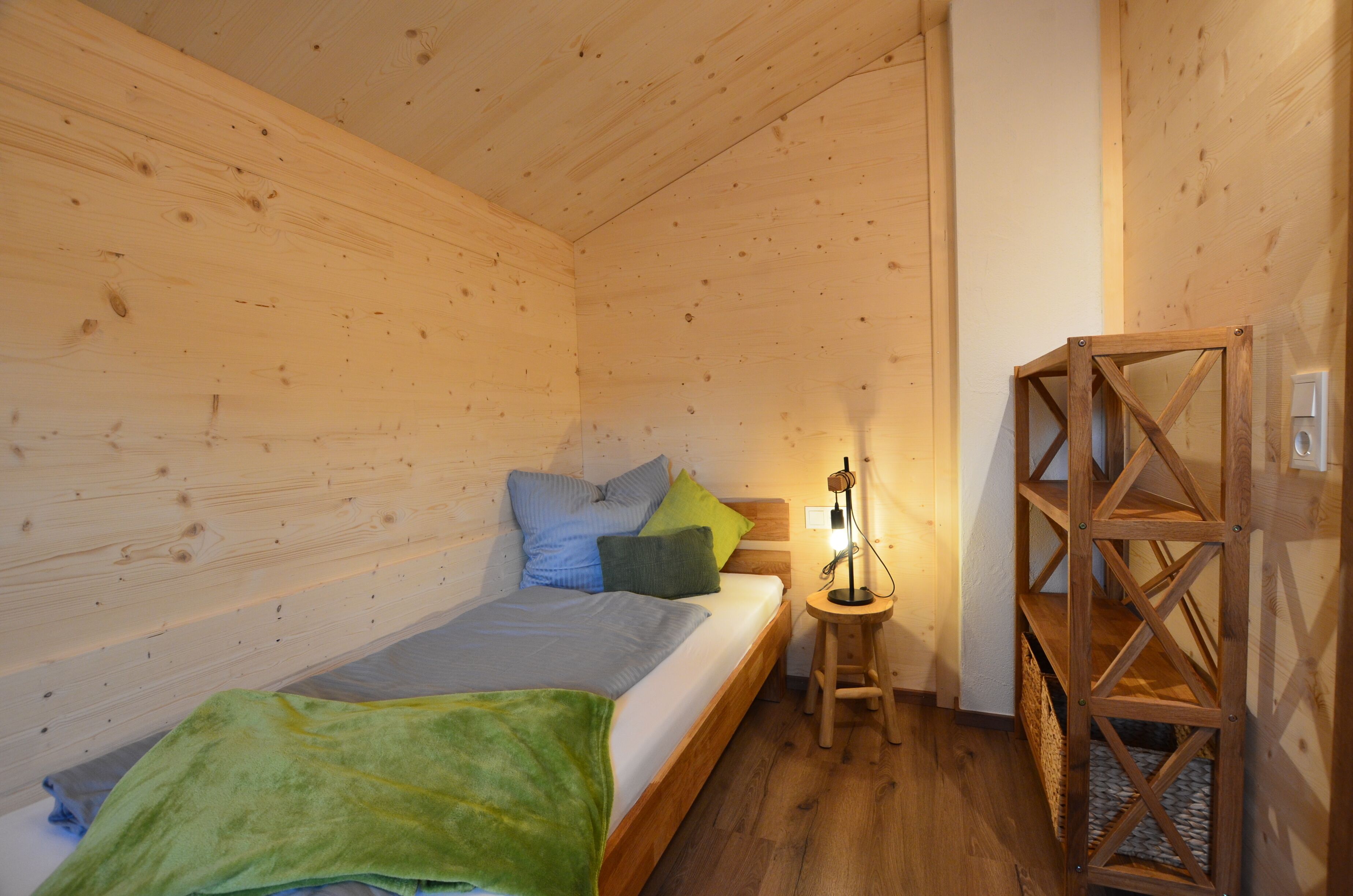 Une pièce de cabane en bois comprenant un lit, des oreillers, une table de chevet et une étagère en bois.
