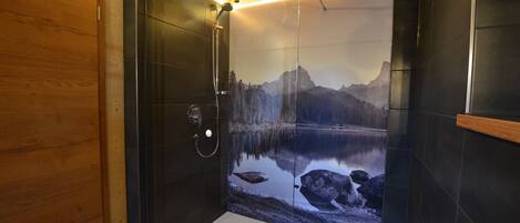 A modern shower with a glass door, a wooden ceiling, and a scenic mural of a mountain lake.