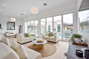 A spacious living room with large windows, a round coffee table, and a modern light fixture.