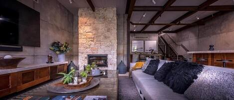 A modern living room with a stone fireplace, a sofa with black pillows, and a television mounted on the wall.