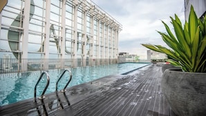 A rooftop pool with a wooden deck, surrounded by glass walls and a large window structure.