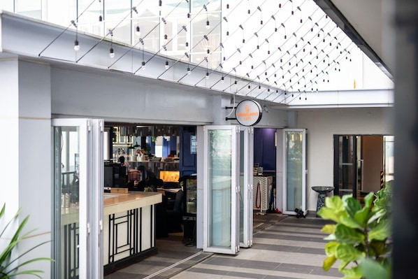 Un vestíbulo de hotel moderno con un separador de vidrio, una recepción y un letrero que indica un restaurante.