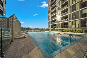 A rooftop pool with a clear view of the city skyline, a modern building with balconies, and a glass fence.