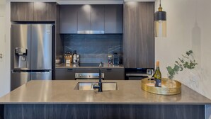 Eine moderne Küche mit einem Edelstahl-Kühlschrank, einem eingebauten Backofen und einer großen Kücheninsel mit Spüle.