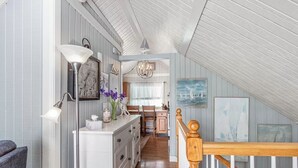Une chambre confortable située dans les combles, avec un escalier en bois, une commode à tiroirs, une lampe et une horloge au mur.