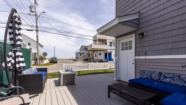 Une terrasse en bois avec des meubles d’extérieur, une clôture blanche et une maison à deux étages en arrière-plan.