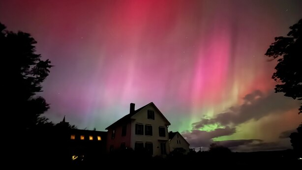A house with a visible chimney and windows, under a night sky with the aurora borealis.