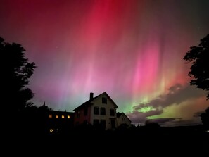A house with a visible chimney and windows, under a night sky with the aurora borealis.