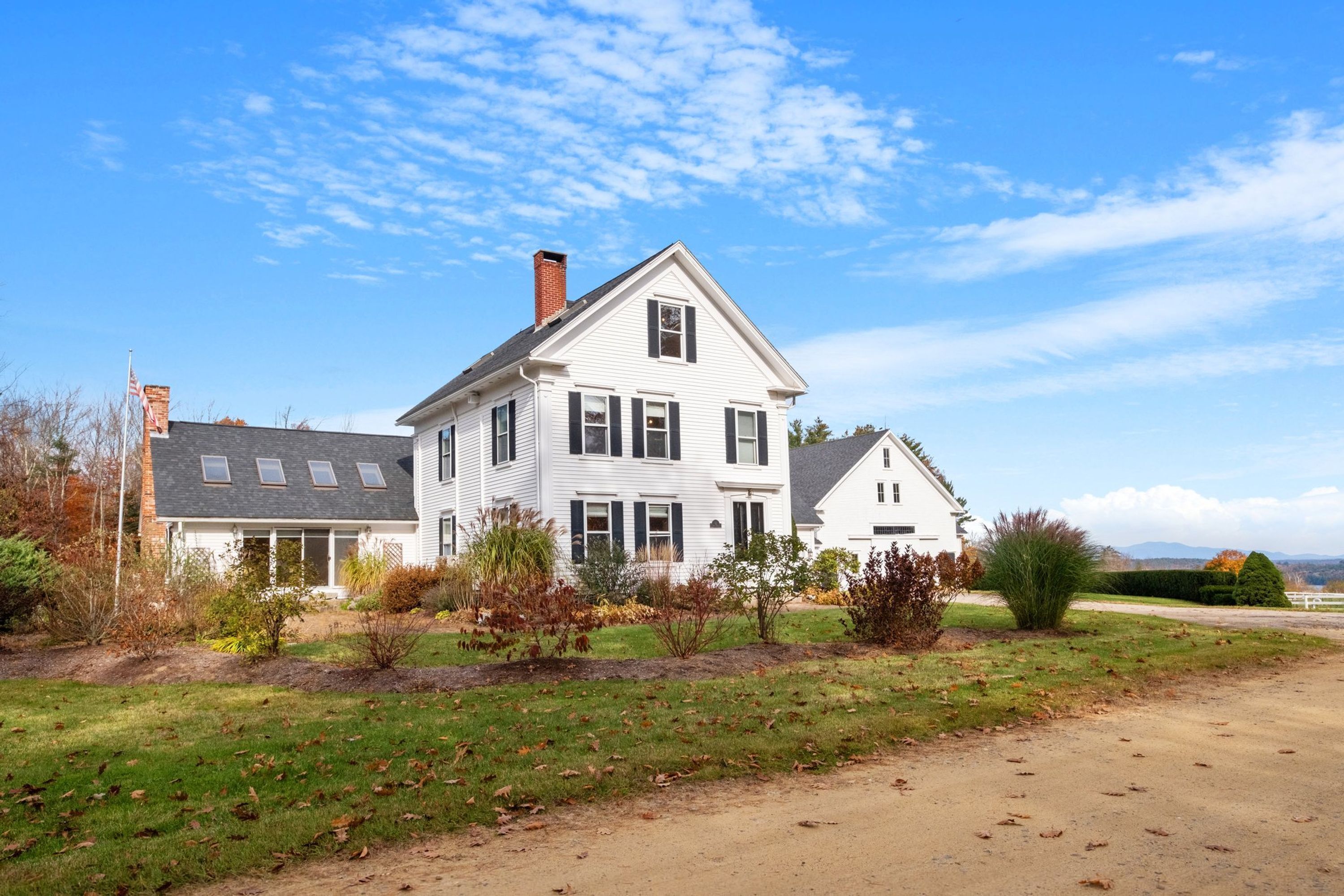 A two-story white house with a gabled roof, a chimney, and a front yard with a dirt path leading to the entrance.