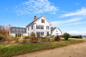 A two-story white house with a gabled roof, a chimney, and a front yard with a dirt path leading to the entrance. - Cozy Stay w Fireplace Near Gunstock Laconia (Sanbornton)