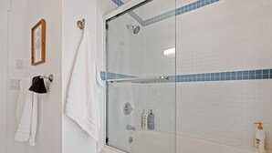 A bathroom with a glass-enclosed shower, white tiled walls, and a white bathtub.