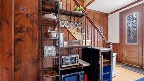 A kitchen with wooden walls, a metal rack holding dishes, a microwave, a toaster, and a refrigerator.