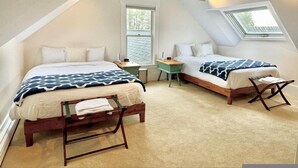 A bedroom with two beds, a small desk, and a window.
