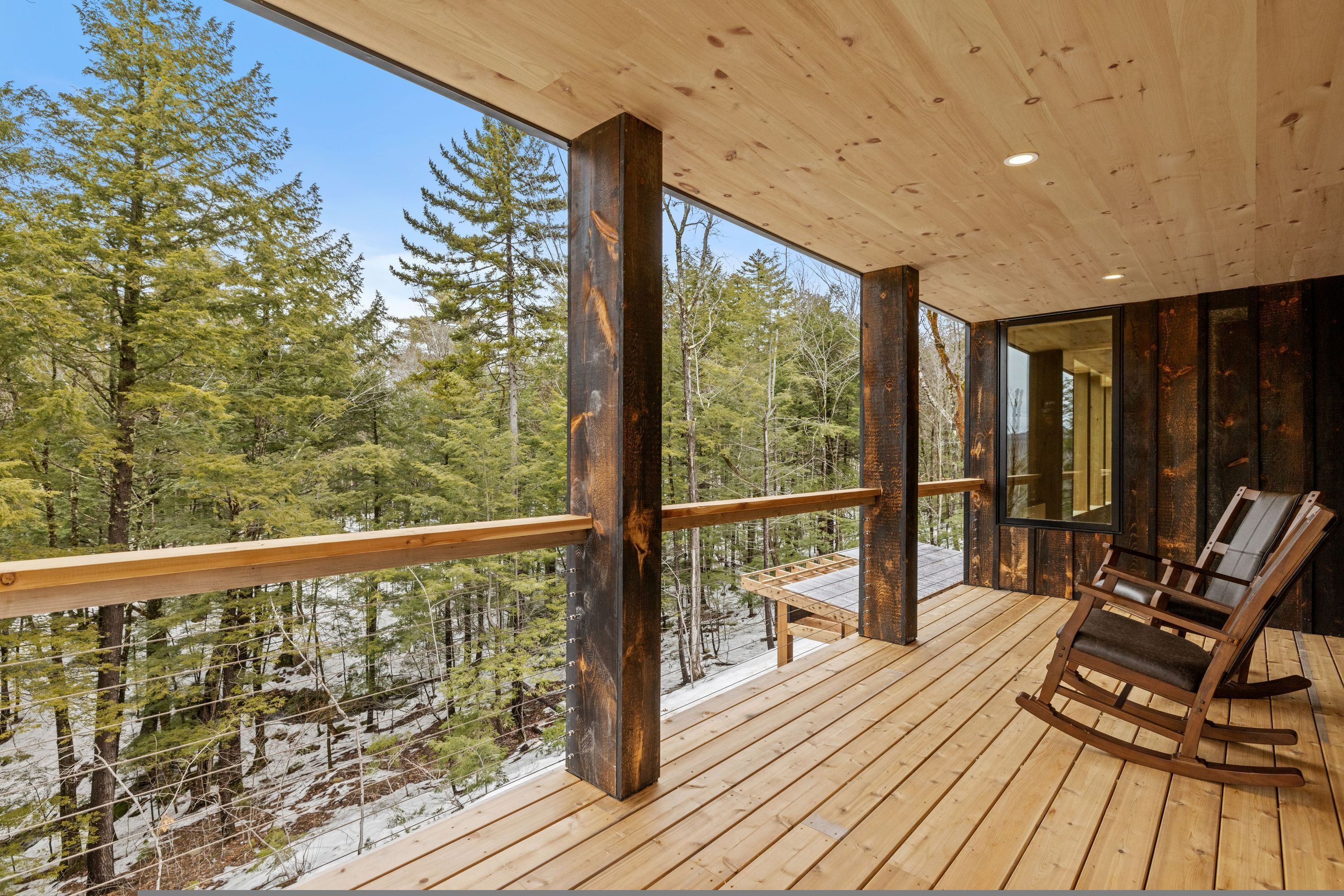 A wooden deck with a rocking chair, wooden railings, and a view of a forest.
