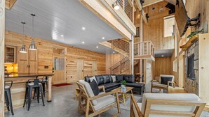 A spacious living area with a wooden interior, a black leather sofa, and a staircase leading to an upper level. - Ski Cabin w Hot Tub Gas Fireplace Near Cranmore (Conway)
