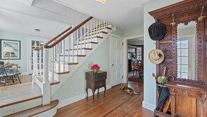 A staircase with white railings and wooden steps, a wooden cabinet with hats, and a cat on the floor.