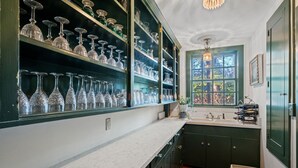 A kitchen with dark green cabinets, a white countertop, and a window with a view of trees.