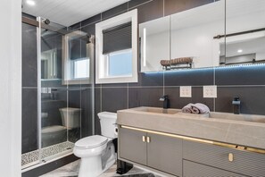 A modern bathroom with a glass-enclosed shower, a toilet, a sink with a vanity, and a large mirror. - New Luxury 4 Bed Condo Perfect for Winter Rental (Hampton)