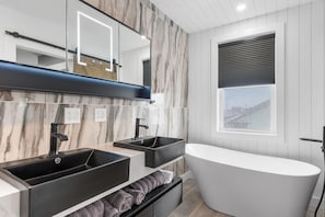 A modern bathroom with a freestanding bathtub, two black sinks, and a large mirror. - New Luxury 4 Bed Condo Perfect for Winter Rental (Hampton)