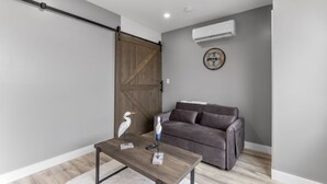 A modern living room with a sliding barn door, a gray sofa, a wooden coffee table, and a wall-mounted air conditioner. - New Luxury 4 Bed Condo Perfect for Winter Rental (Hampton)