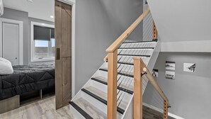 A modern bedroom with a bed, a wooden door, and a staircase with a wooden railing. - New Luxury 4 Bed Condo Perfect for Winter Rental (Hampton)