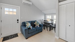 A modern living room with a blue sofa, a dining table with chairs, a white door, and a white closet. - Modern Condo Perfect For Winter Rental (Hampton)