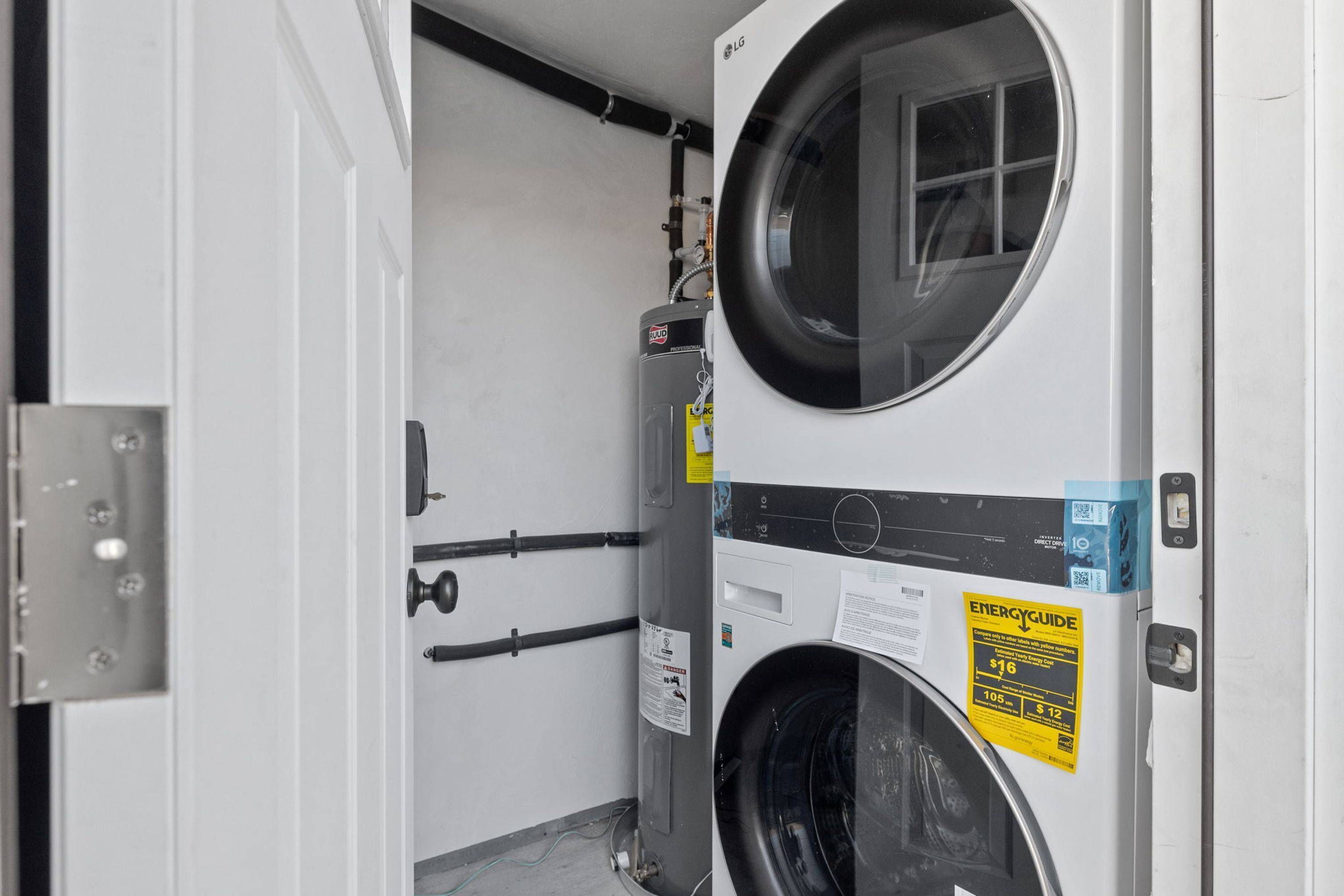 A laundry room with a front-loading washer and dryer, a water heater, and a door with a metal handle.