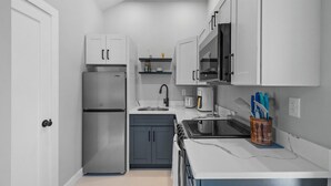 A compact kitchen with white cabinets, a stainless steel refrigerator, a microwave, and a coffee maker. - Modern Condo Perfect For Winter Rental (Hampton)