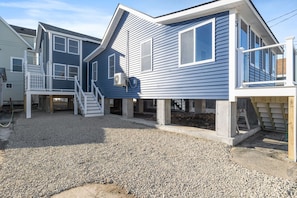 A two-story house with a gravel driveway, a front porch, and a staircase leading to the second floor. - Modern Condo Perfect For Winter Rental (Hampton)