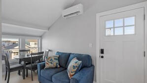 A modern living room with a blue sofa, a dining table with chairs, and a white door with a window. - Modern Condo Perfect For Winter Rental (Hampton)