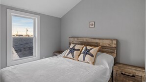 A bedroom with a large window, a wooden headboard, and starfish pillows. - Modern Condo Perfect For Winter Rental (Hampton)