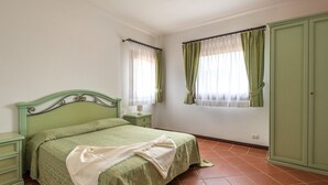 Ein Schlafzimmer mit einem grünen Bett, zwei Nachttischen, einem Schrank und zwei mit Vorhängen versehenen Fenstern.