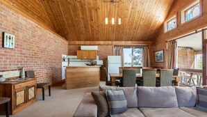 A cozy cabin interior with a wooden ceiling, brick walls, a dining area with a table and chairs, and a sofa.