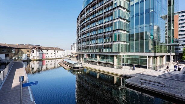 A modern building with a glass facade, a canal, and a wooden walkway. - Zen By The Water, by Veeve (London)
