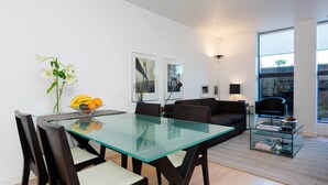 A modern living room with a glass dining table, dark wooden chairs, a black sofa, and a glass coffee table. - Zen By The Water, by Veeve (London)