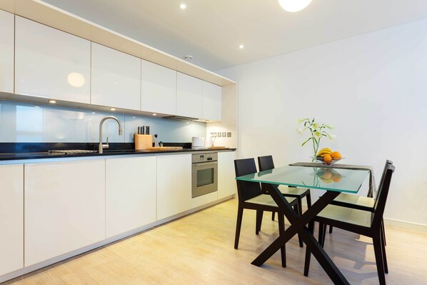 A modern kitchen with white cabinets, stainless steel appliances, and a glass dining table with black chairs.