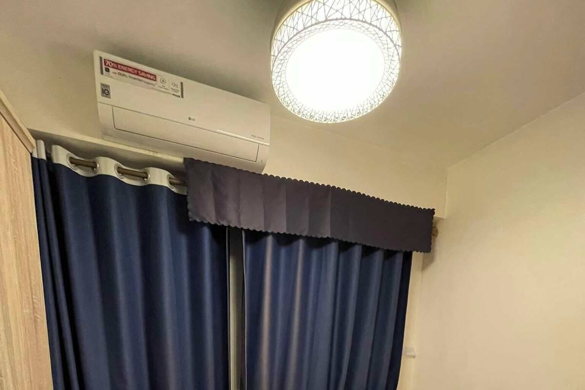 A bedroom with a bed, a window with curtains, an air conditioning unit, and a mosquito net on the floor.