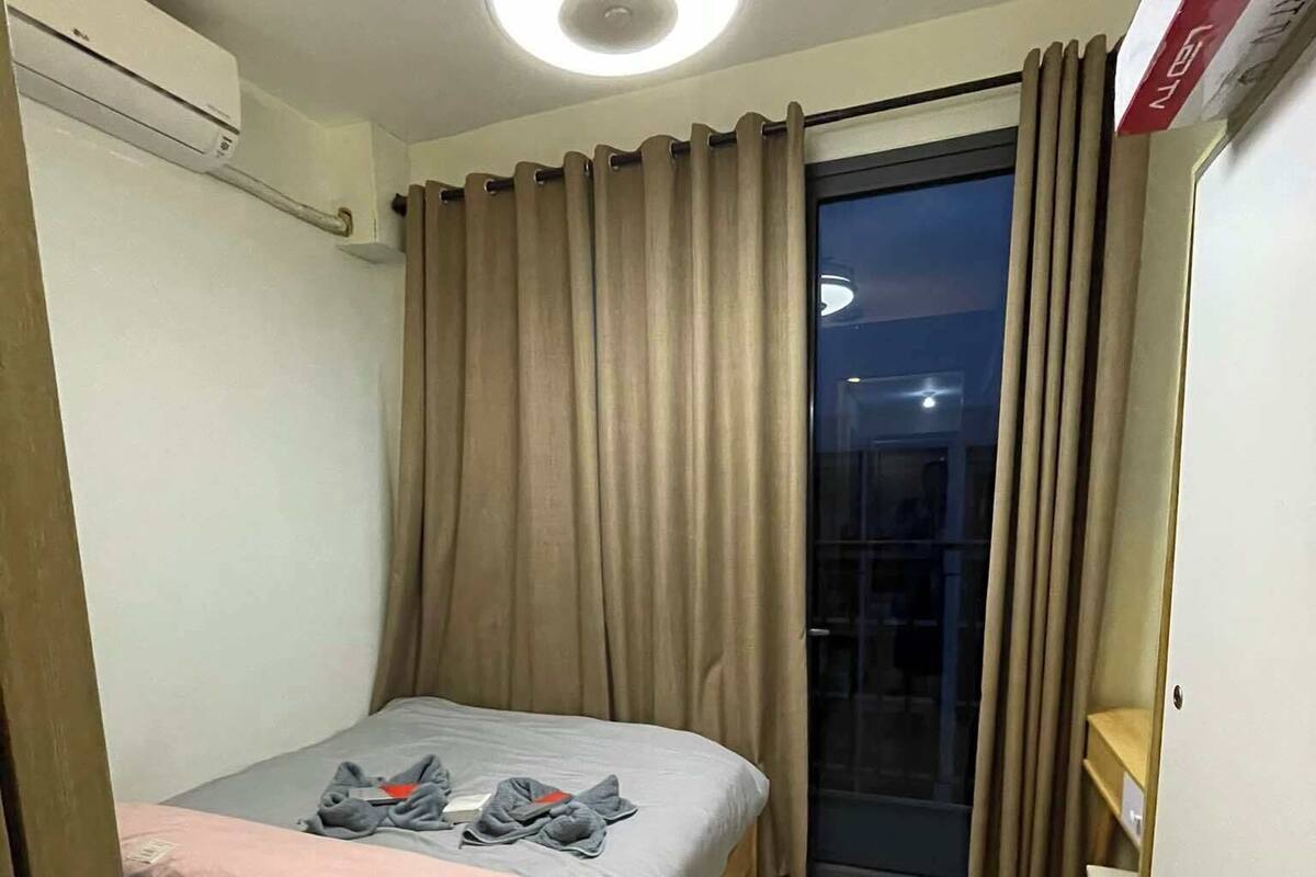 A small, well-lit room with a single bed, a ceiling fan, and a sliding glass door leading to a balcony.