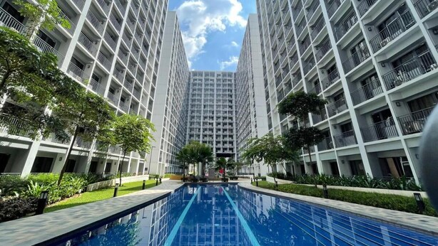 Un immeuble résidentiel moderne doté d’une piscine centrale, entouré de verdure et agrémenté de balcons en hauteur.