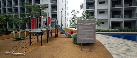 Un parque infantil con diversos juegos, incluyendo toboganes y estructuras para escalar, rodeado por un edificio con varios balcones.
