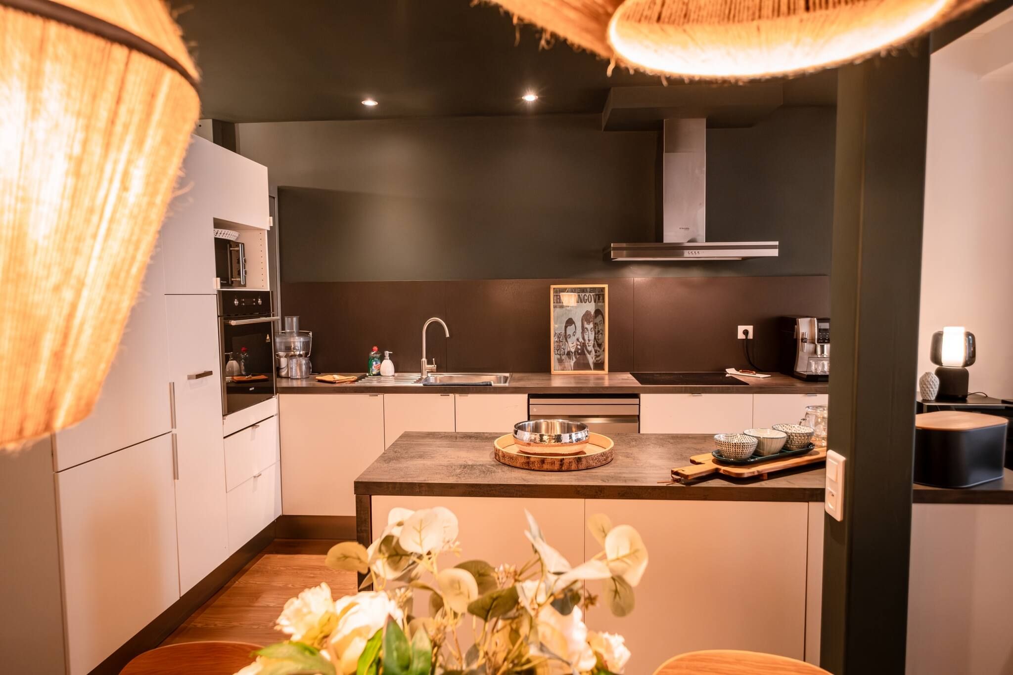 Une cuisine moderne dotée d’un îlot central, d’appareils électroménagers en acier inoxydable et d’un luminaire suspendu.