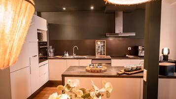 Une cuisine moderne dotée d’un îlot central, d’appareils électroménagers en acier inoxydable et d’un luminaire suspendu.
