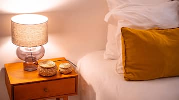 A neatly made bed with white and yellow pillows, a bedside lamp, and two woven baskets on a wooden nightstand.