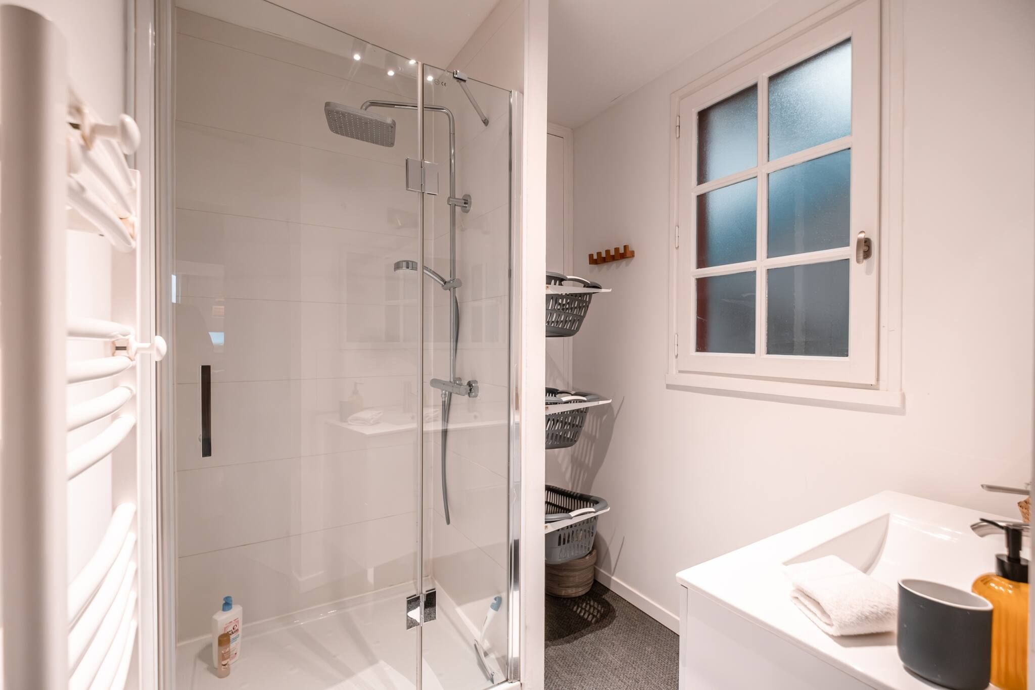 Ein modernes Badezimmer mit einer gläsernen Duschkabine, weißen Fliesen, einem weißen Waschbecken und einem Fenster mit Milchglas.